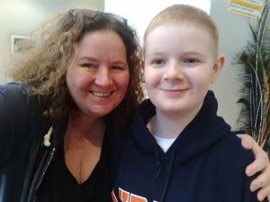 Siobhan and Conor taking a selfie. both smiling and looking at the camera. Conor is feeling embarrassed of his mum trying to take a photo